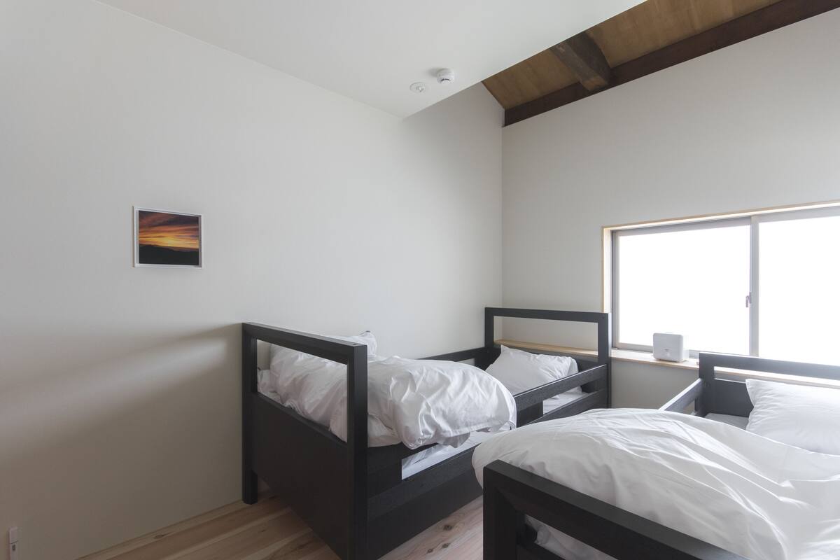 Een slaapkamer met twee bedden, een raam en een klein schilderij aan de muur.