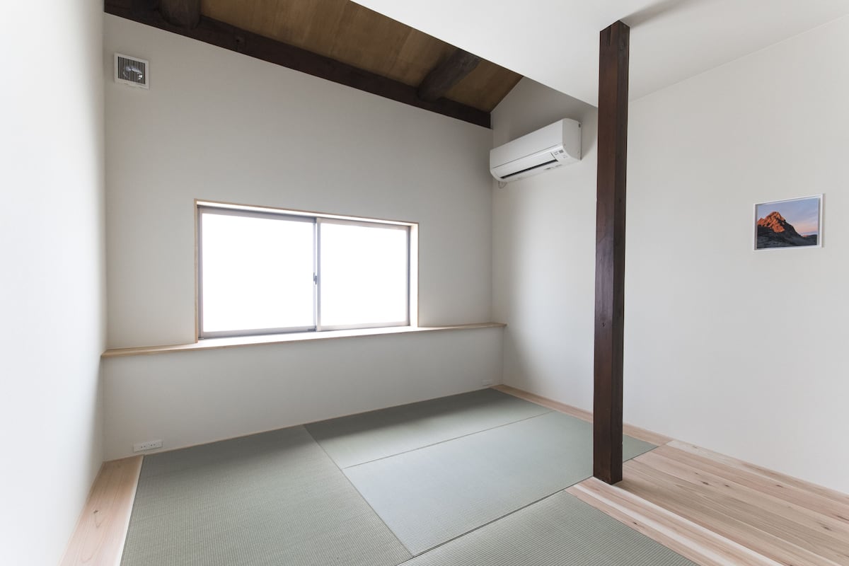 Een kamer met tatami vloerbedekking, een raam en een wandairconditioner.
