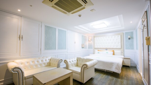 Una habitación de hotel con una cama, dos sofás blancos, una mesita y una ventana con persianas.