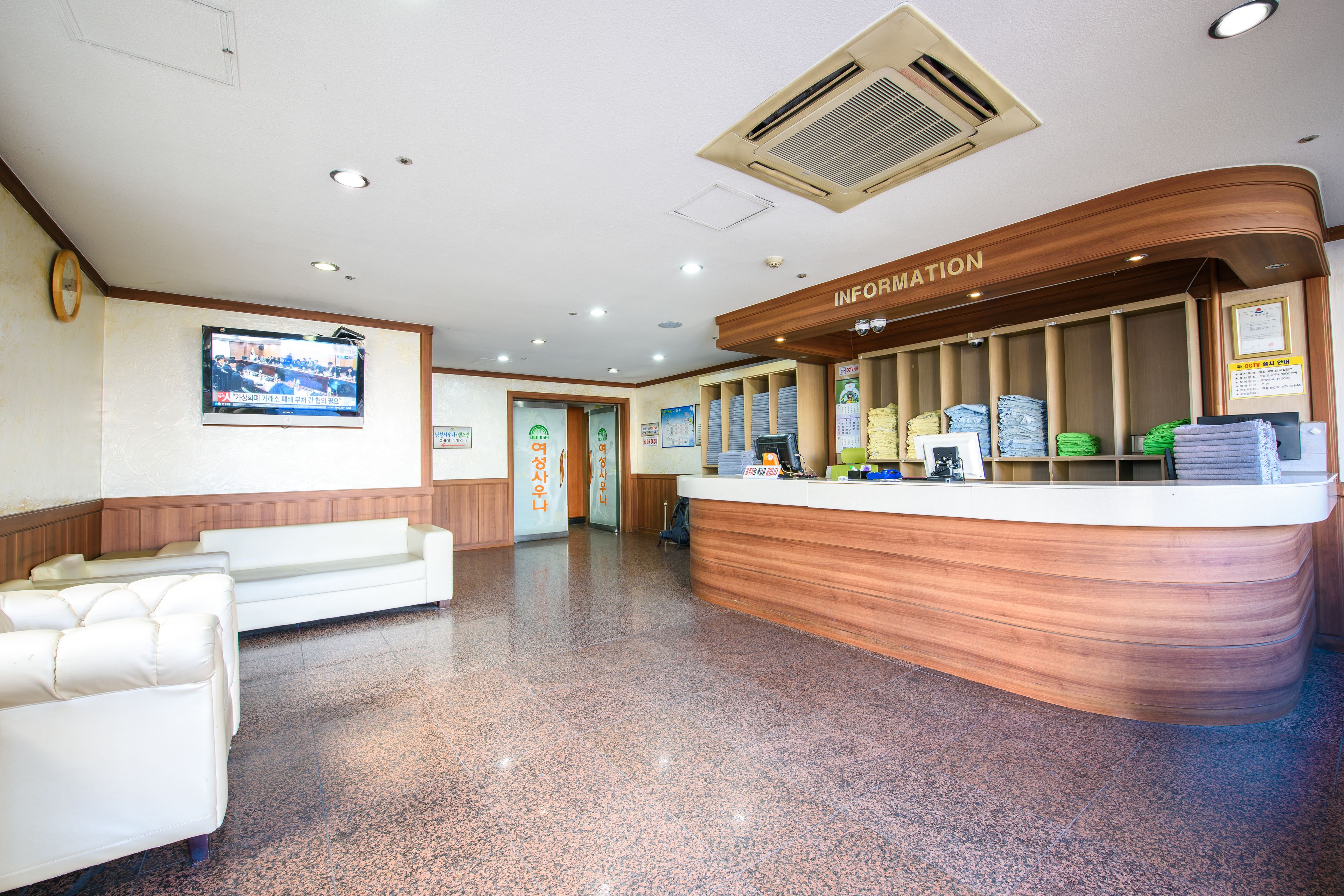 A reception area with a wooden counter, white sofas, and a television on the wall.