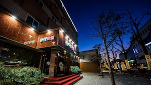 Un hotel con alfombra roja en la entrada, un cartel con texto en coreano y fachada de ladrillo.