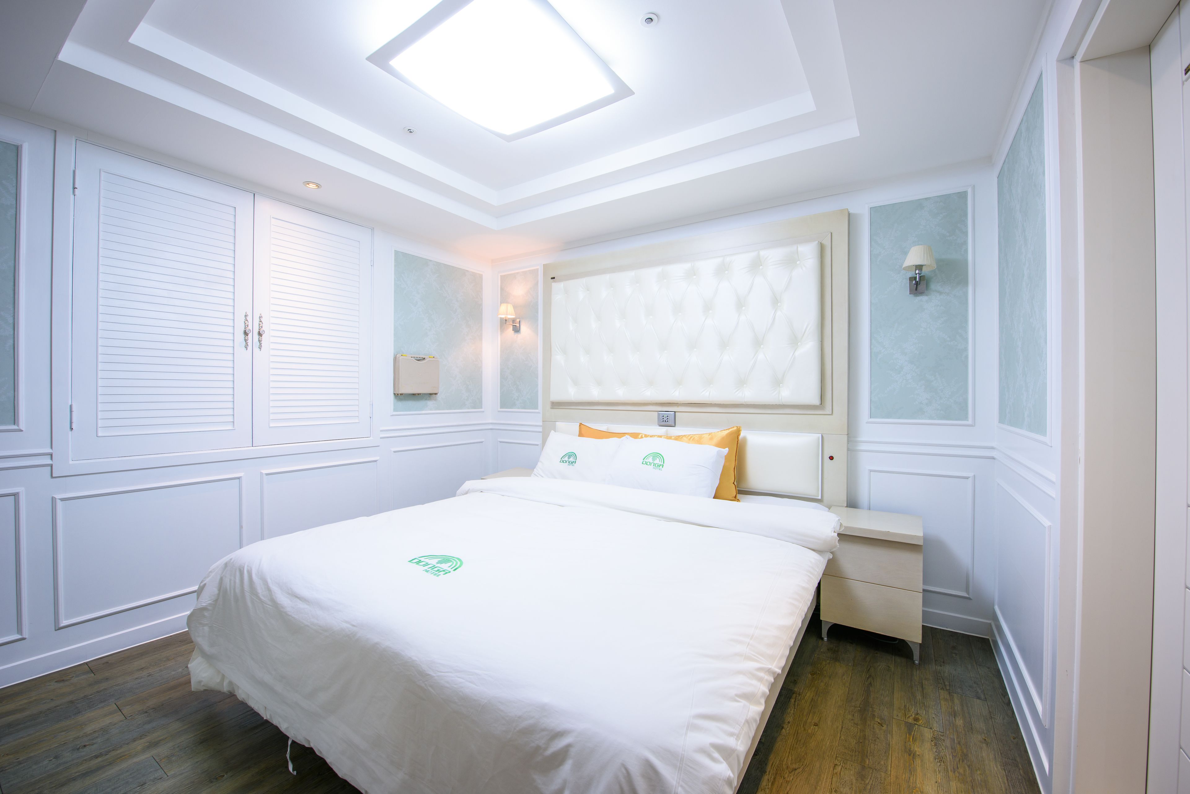 Camera d'albergo con un letto grande, un comodino, una lampada a parete e una luce a soffitto.