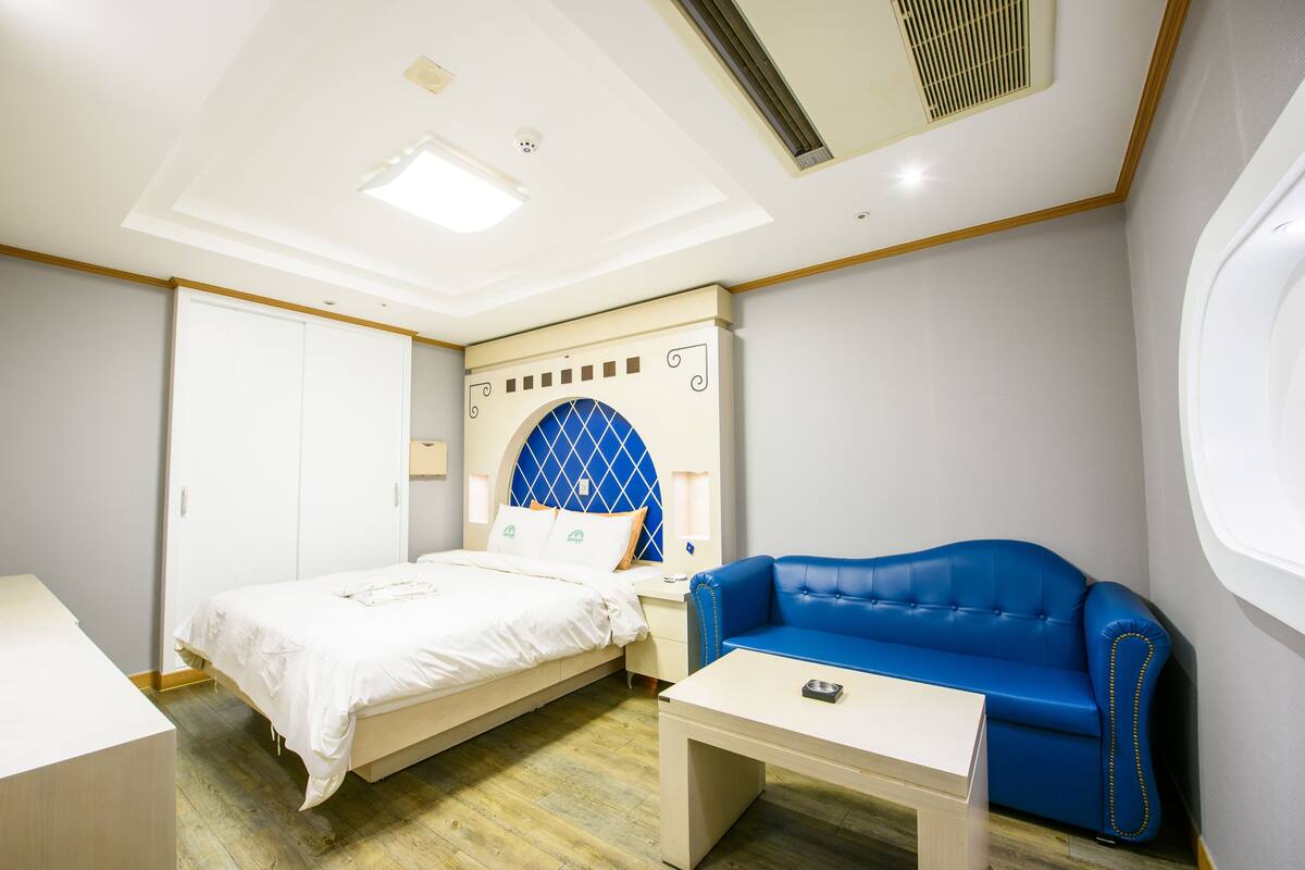 Una habitación de hotel con una cama, un sofá azul, una mesita y un armario.