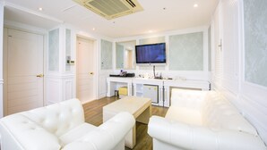 Una sala de estar moderna con muebles blancos, un televisor de pantalla plana y una kitchenette.