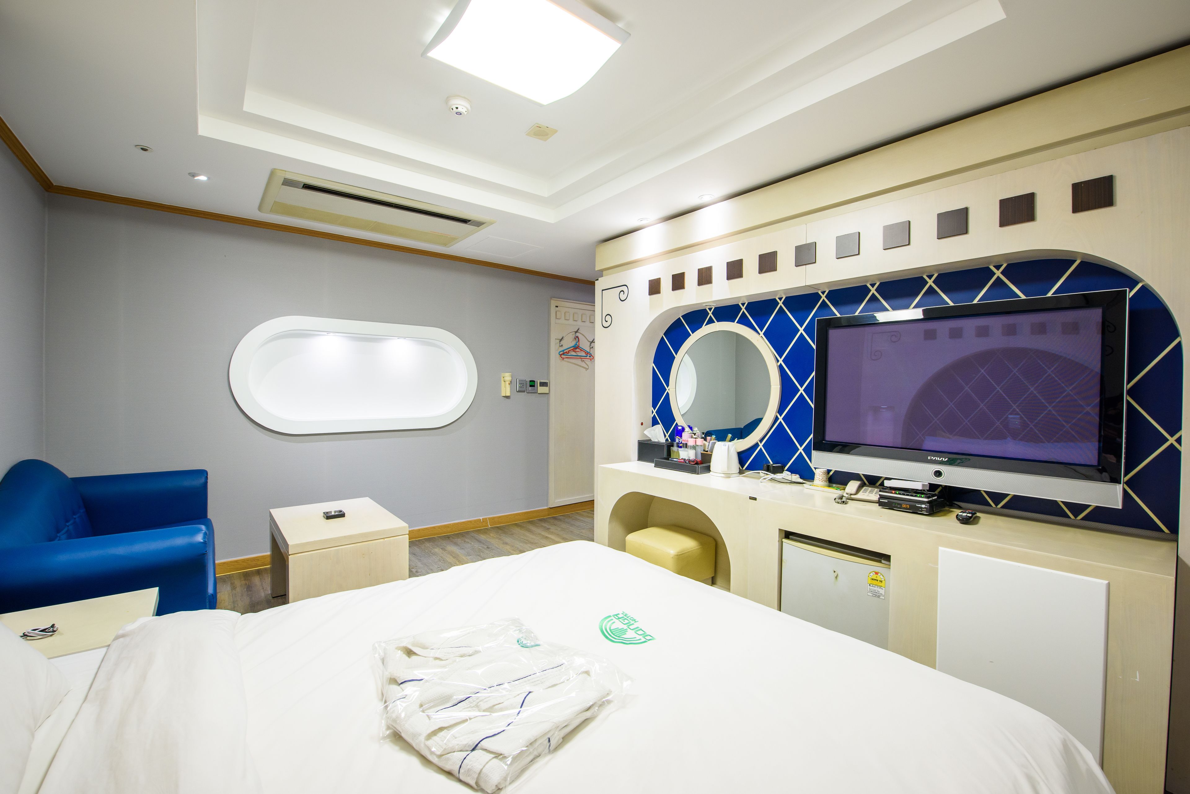 A hotel room with a bed, a blue chair, a television, a small desk, and a window.