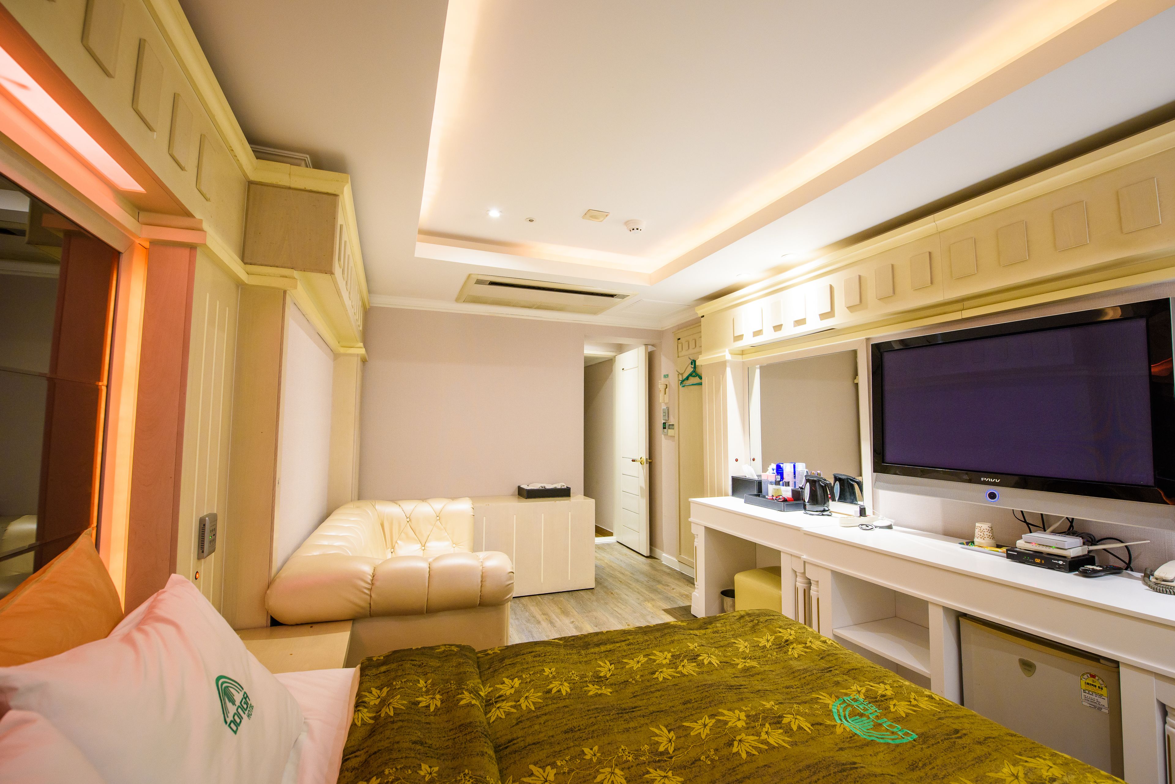A hotel room with a bed, a desk with a flat-screen TV, a seating area, and a bathroom.