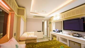 A hotel room with a bed, a desk with a flat-screen TV, a seating area, and a bathroom.