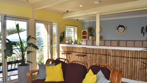 A room with a wicker sofa, a large potted plant, and a bamboo wall. - Mad Monkey Coogee Beach Hostel (Coogee)