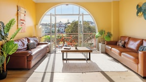A spacious living room with two leather sofas, a wooden coffee table, and large windows offering a city view. - Mad Monkey Coogee Beach Hostel (Coogee)