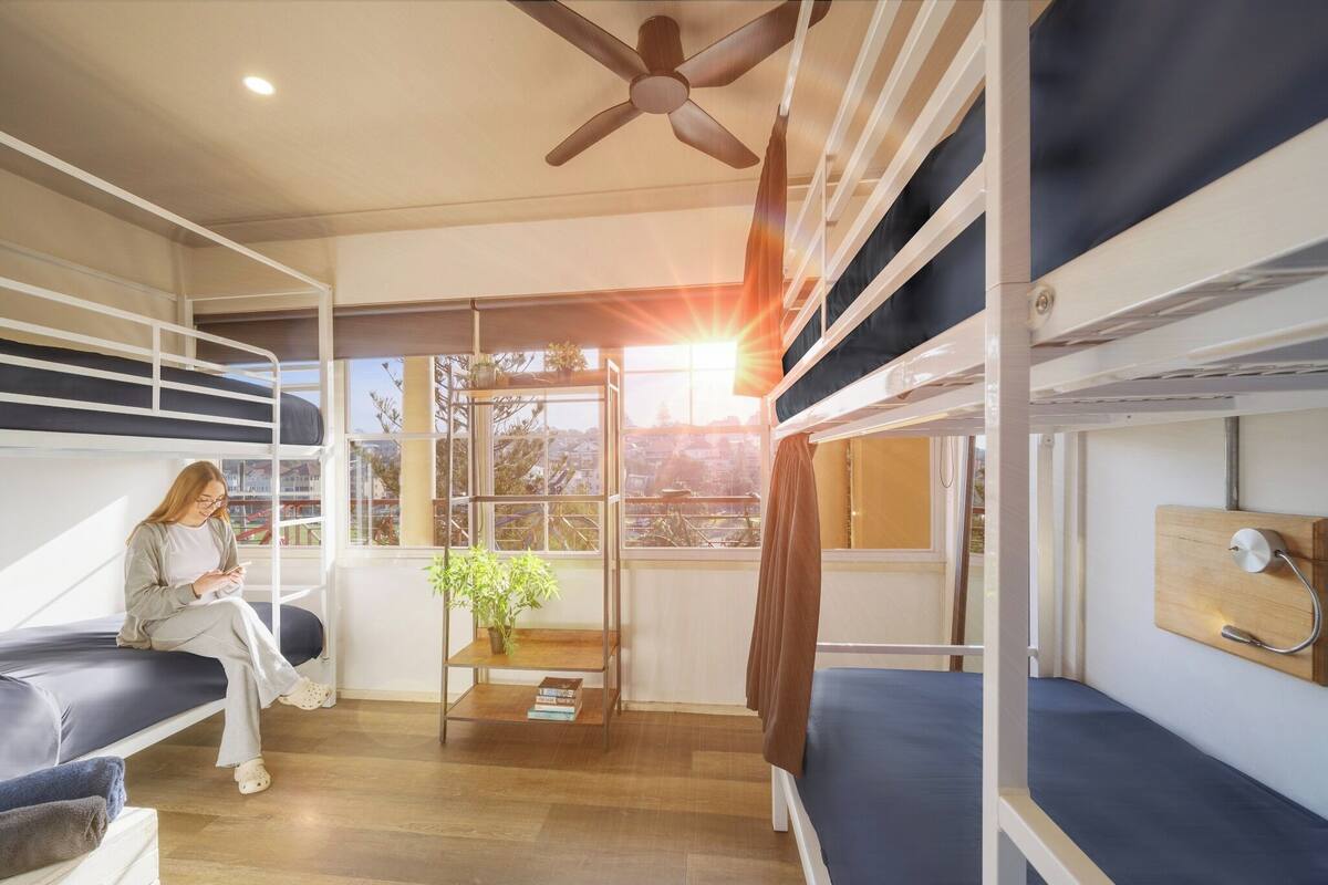 A bunk bed room with a ceiling fan, a window with a view, and a small table with a plant.