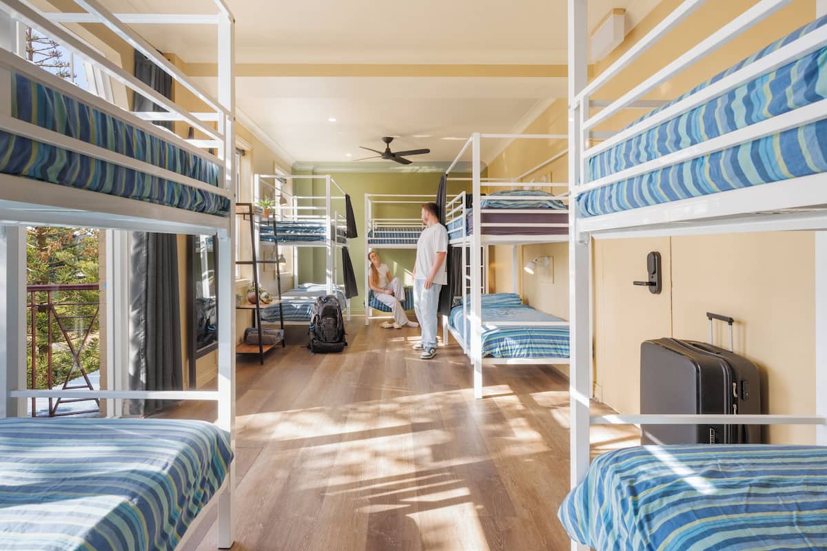 A dormitory room with bunk beds, a ceiling fan, and a suitcase on the floor.