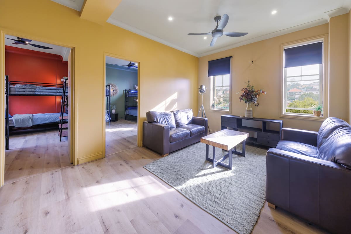 A living room with a sofa, a coffee table, and a TV. There is a window with a view of the city.