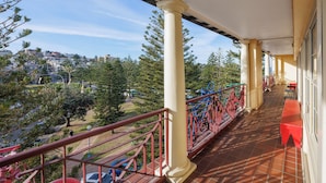 A balcony with red railings, a tiled floor, and a view of a residential area with trees and parked cars. - Mad Monkey Coogee Beach Hostel (Coogee)