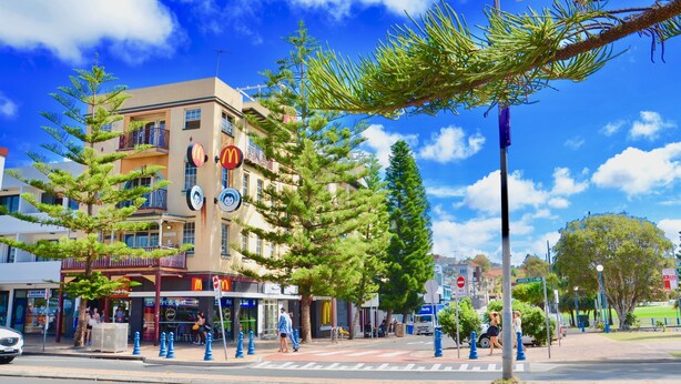 Um edifício com vários andares, área externa para restaurante e céu azul com nuvens.