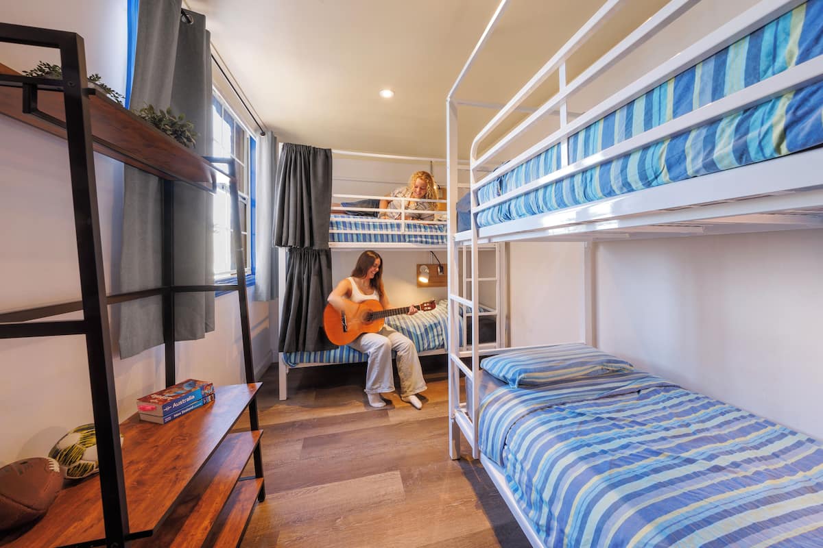 A dormitory room with bunk beds, a wooden bench, and a small table with a book and a football.