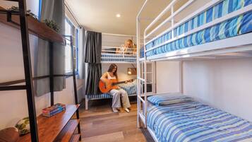 A dormitory room with bunk beds, a wooden bench, and a small table with a book and a football.
