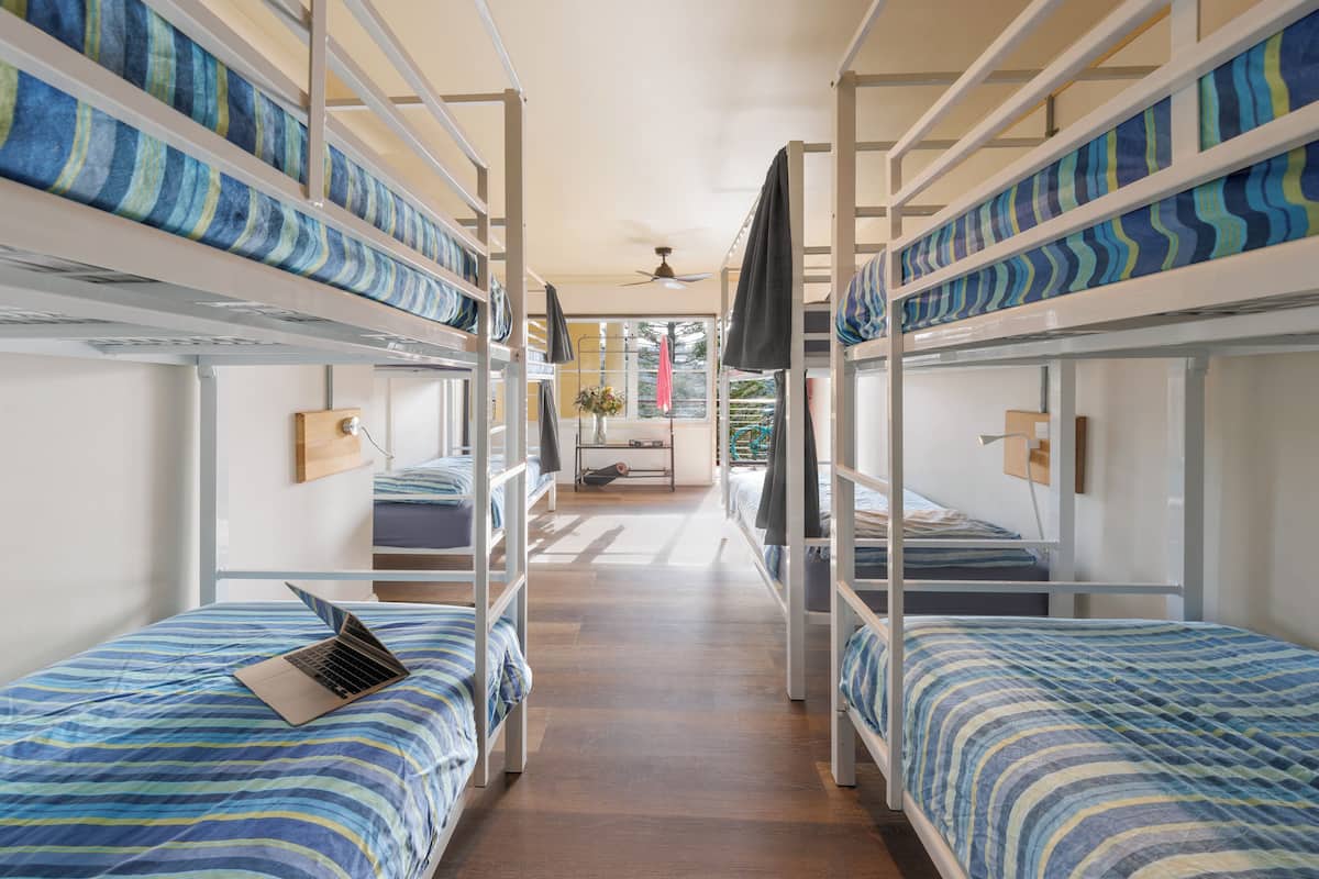 A bunk bed room with a laptop on one bed, a ceiling fan, and a window with a view.