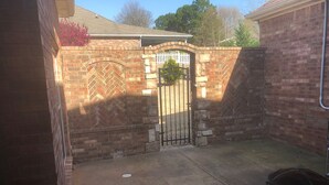 Un garage en briques avec une entrée fermée par un portail, une allée en béton et un pot en métal posé sur le sol.