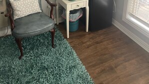 Une pièce comprenant un fauteuil à revêtement gris, une petite table d’appoint blanche avec une lampe, un four à micro-ondes et une poubelle.