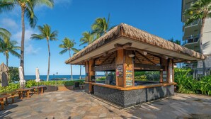 A beachside kiosk with a thatched roof, stone flooring, and a view of the ocean. - Discover Ko Olina: Exclusive Deals on Your Dream Vacation in Our 2BR Condo (Kapolei)