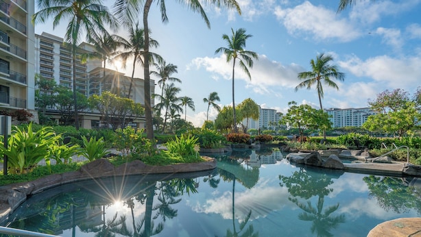 A resort pool surrounded by palm trees and hotel buildings. - Discover Ko Olina: Exclusive Deals on Your Dream Vacation in Our 2BR Condo (Kapolei)
