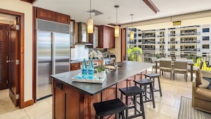 A modern kitchen with a large island, bar stools, and a view of a multi-story building. - Discover Ko Olina: Exclusive Deals on Your Dream Vacation in Our 2BR Condo (Kapolei)