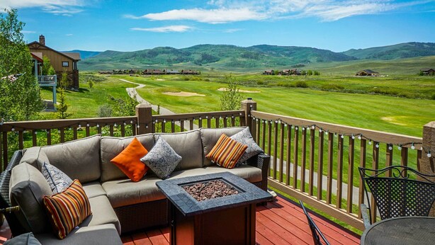 Um terraço com sofá e lareira, com vista para um campo de golfe e colinas.