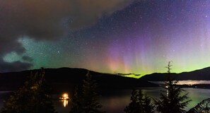 Nachtszene mit Sternenhimmel, Polarlichtern und Lagerfeuer am See.