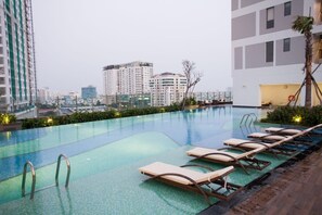 A rooftop swimming pool with lounge chairs and a view of surrounding high-rise buildings. - Trang's Apartment (Ho Chi Minh City)