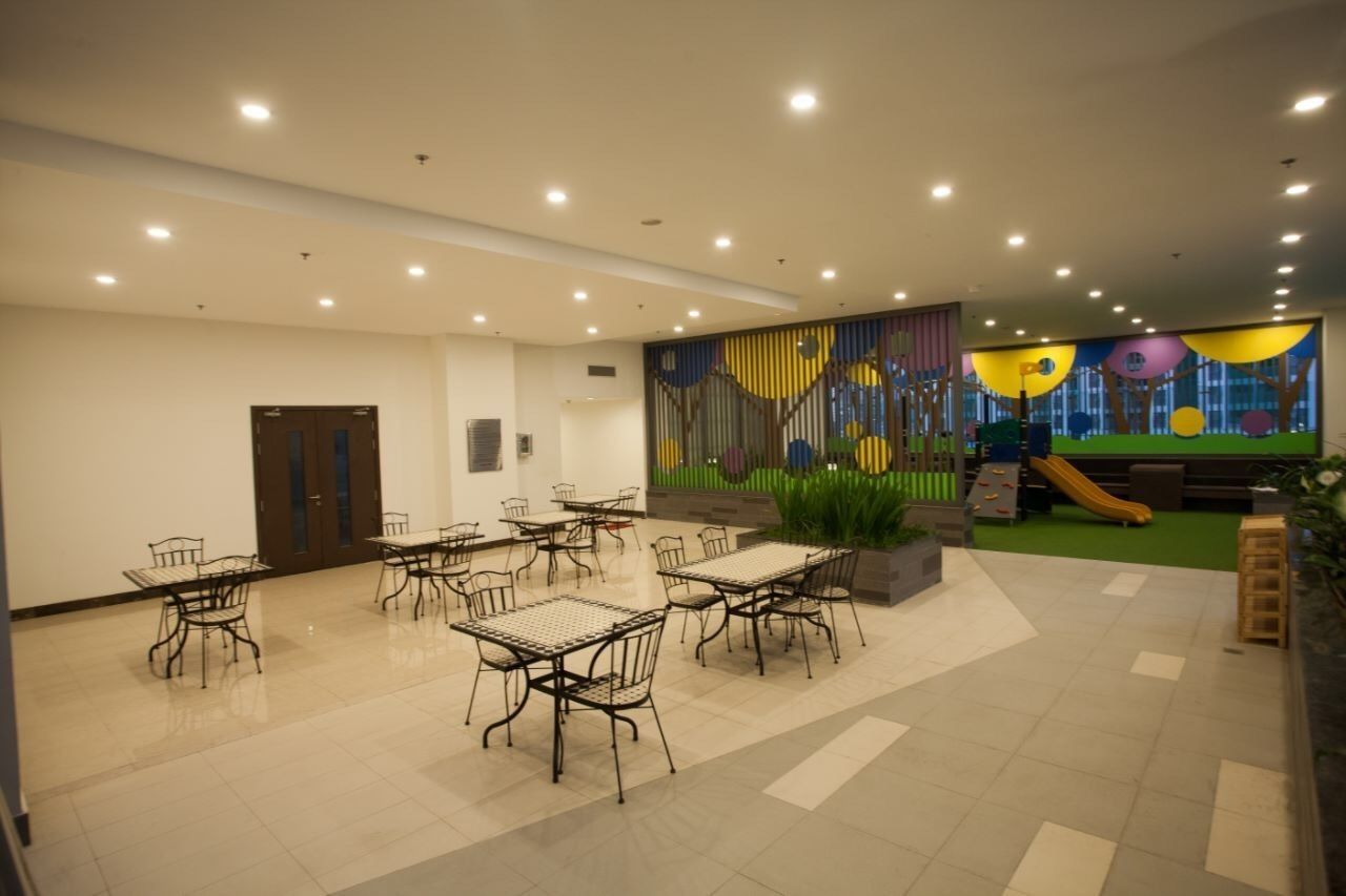 A spacious indoor area with tables and chairs, a children's play area with a slide, and a mural on the wall.