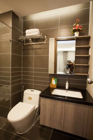 A modern bathroom with a toilet, sink, and mirror. There is a shelf with towels and a small vase with flowers. - Trang's Apartment (Ho Chi Minh City)
