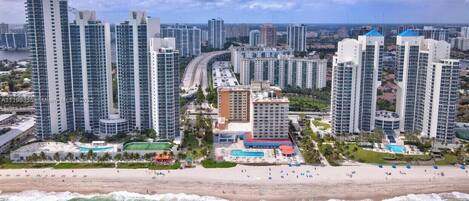 A coastal cityscape with high-rise buildings, a beach, and a marina.