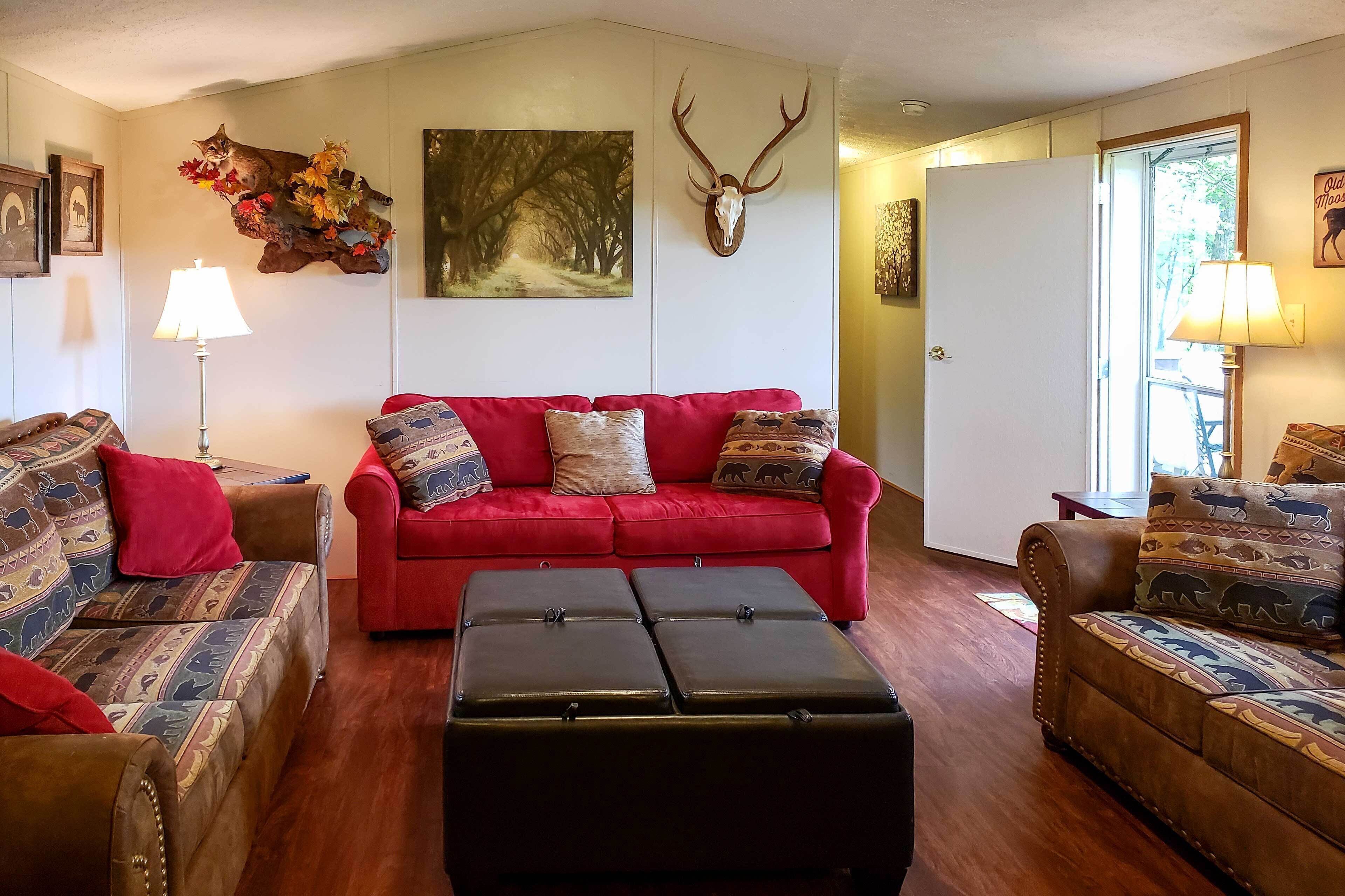 A living room with a red sofa, patterned armchairs, a wooden coffee table, and a mounted deer skull.