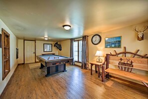 A pool table in a room with wooden flooring, a clock on the wall, and a deer skull decoration.