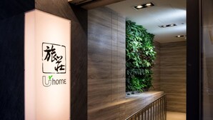 Un área de recepción con un mostrador de madera, un jardín vertical y un letrero con caracteres japoneses y la palabra "Uhome".