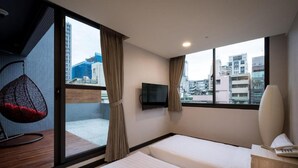 Habitación de hotel con cama, televisor, sillón colgante y vistas a la ciudad.