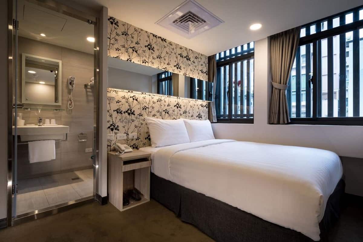 A hotel room with a bed, a bathroom with a mirror, a sink, and a window with curtains.