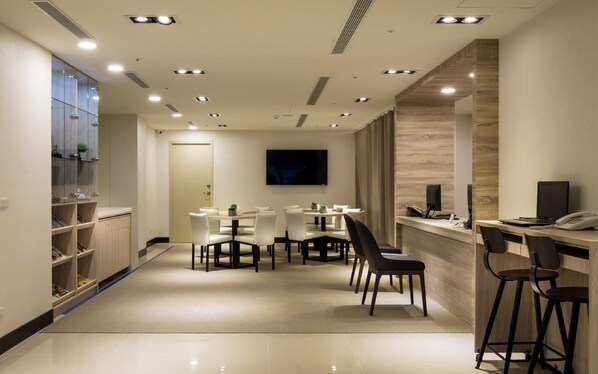 A modern hotel lobby with a reception desk, seating area, and a TV screen.