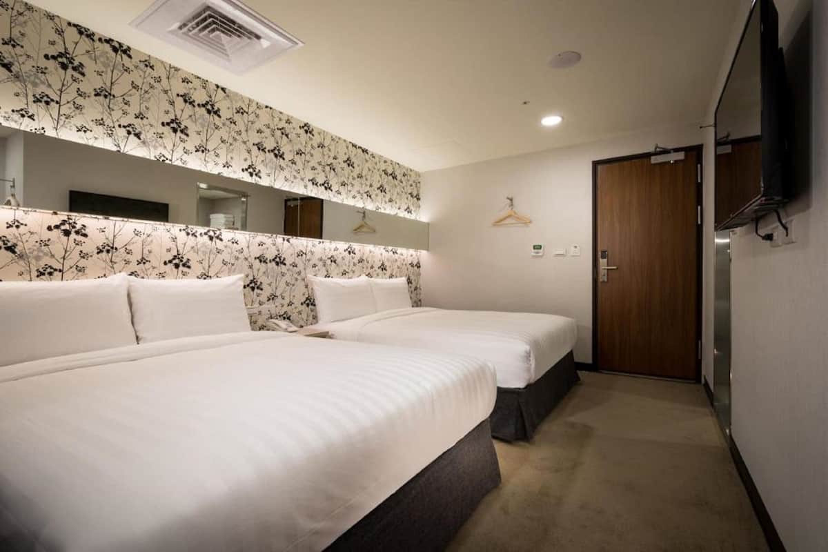 A hotel room with two beds, a large mirror, a wooden door, and a television mounted on the wall.