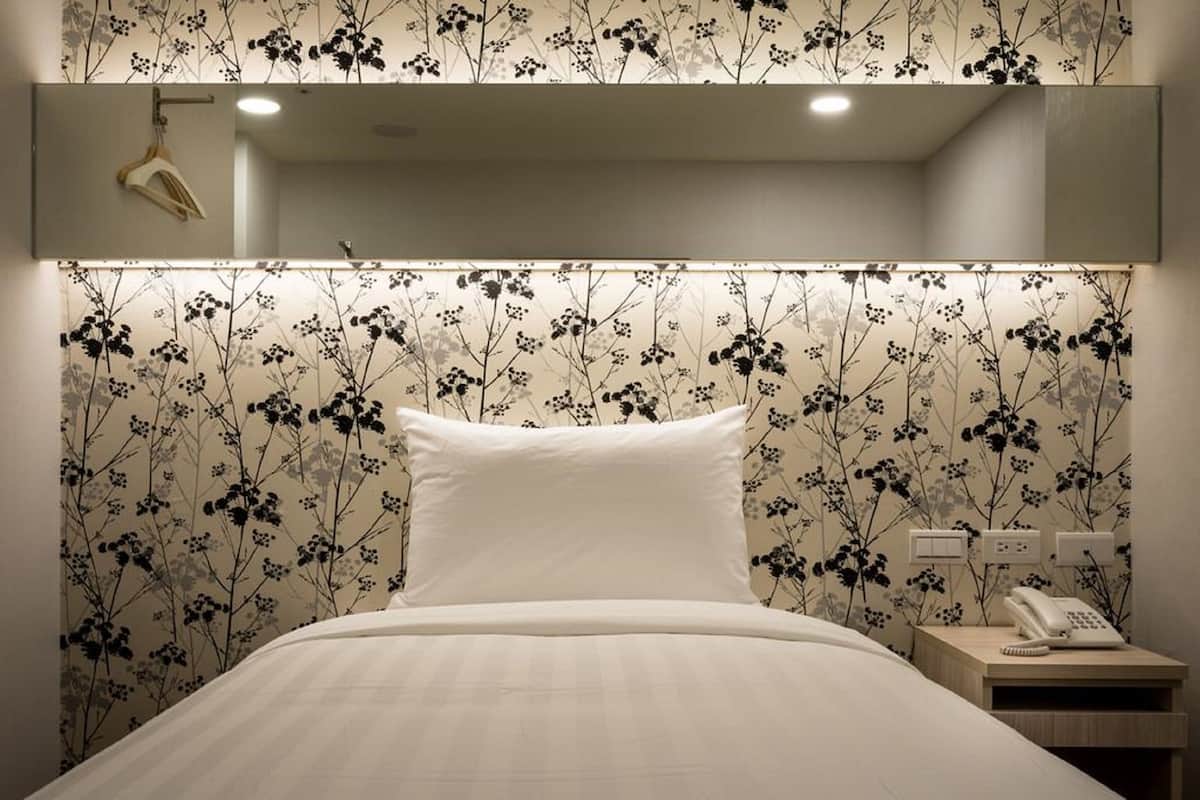 A hotel room with a bed, a nightstand, a telephone, and a mirror above the bed.