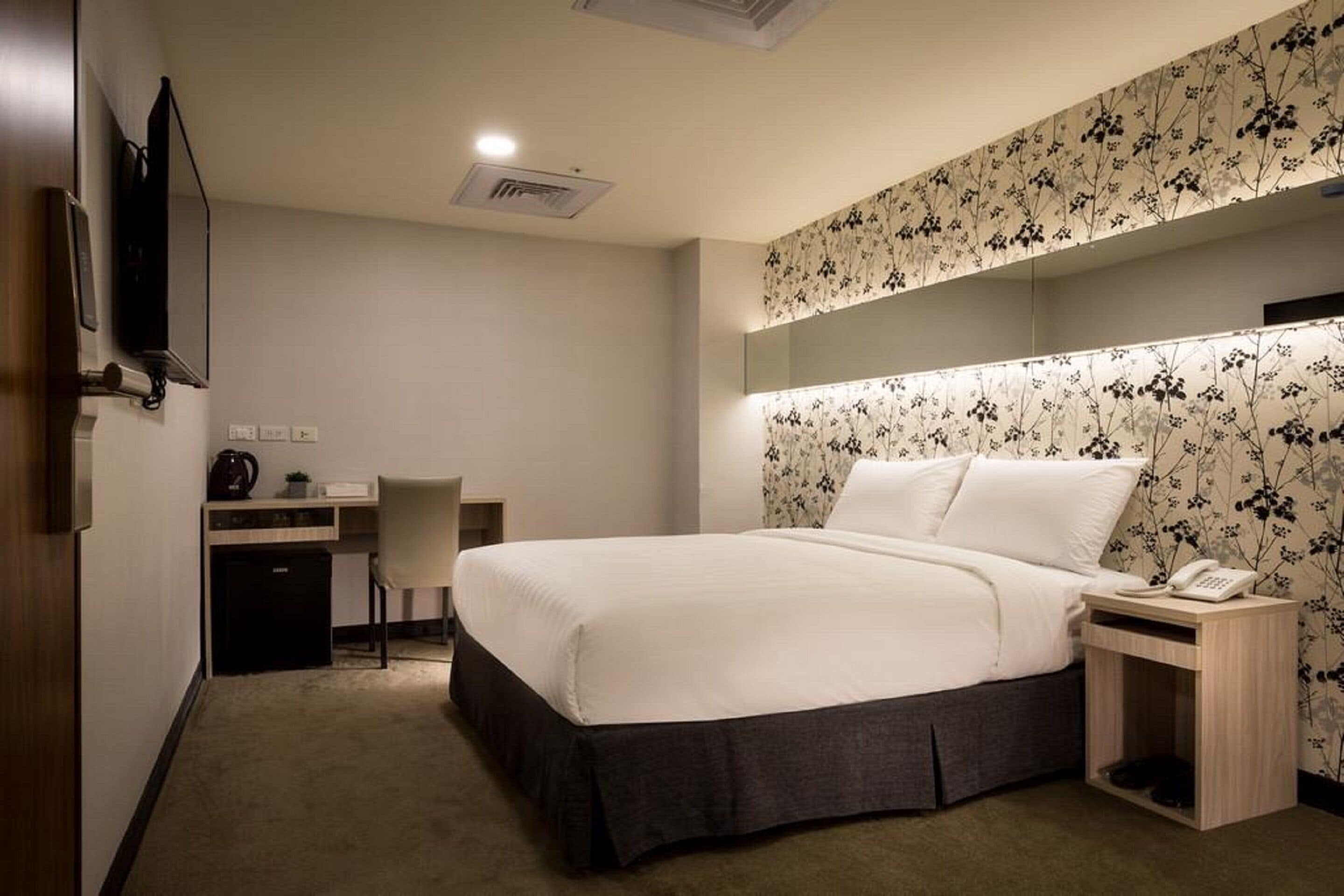 Een hotelkamer met een bed, een bureau, een stoel, een nachtkastje en een telefoon.