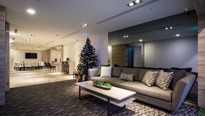 Una sala moderna con un sofá grande, una mesita de centro y un árbol de Navidad. Se aprecia un comedor al fondo, con una mesa larga y sillas.