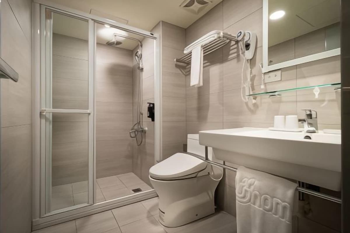 A modern bathroom with a glass shower enclosure, a toilet, and a sink with a towel rack.