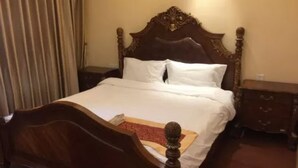 Una cama de madera con cabecera, ropa de cama blanca y una mesita de noche con cajones.
