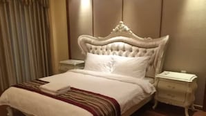 Una cama bien hecha con edredón blanco y manta a rayas, dos mesitas de noche con lámparas y un cabecero de madera.