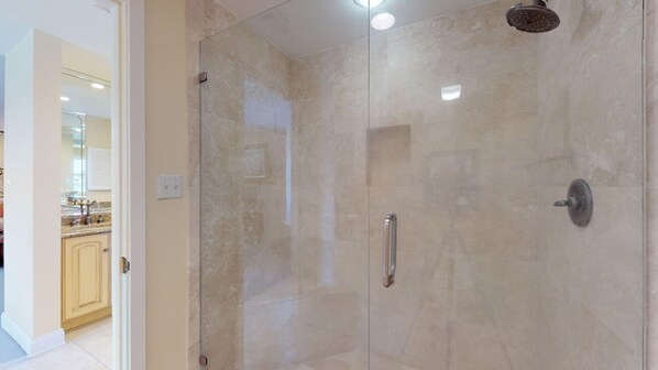 A glass-enclosed shower with a handheld showerhead and a wall-mounted control.