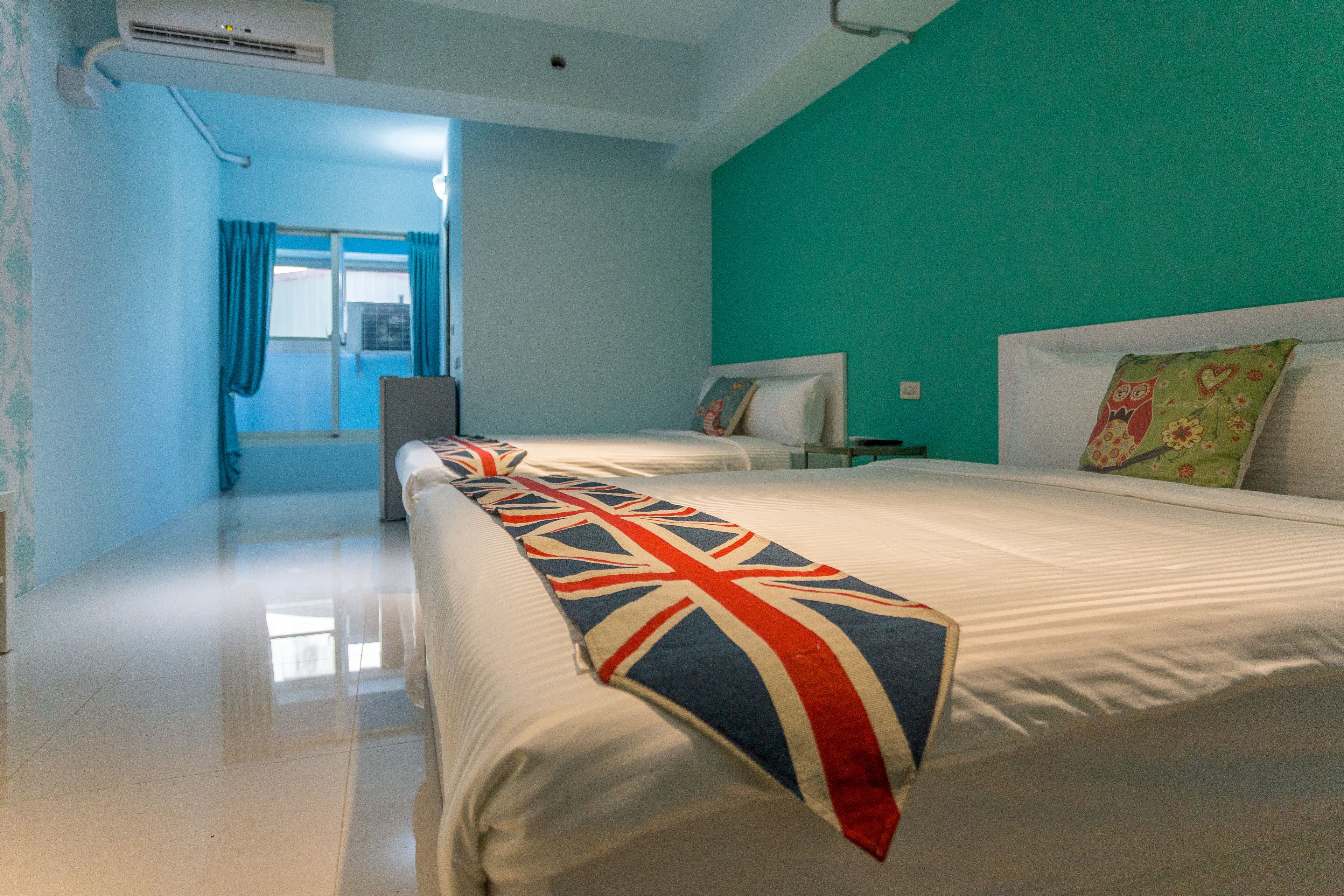 Ein Hotelzimmer mit einem großen Bett, einem kleineren Bett und einem Fenster mit Vorhängen.