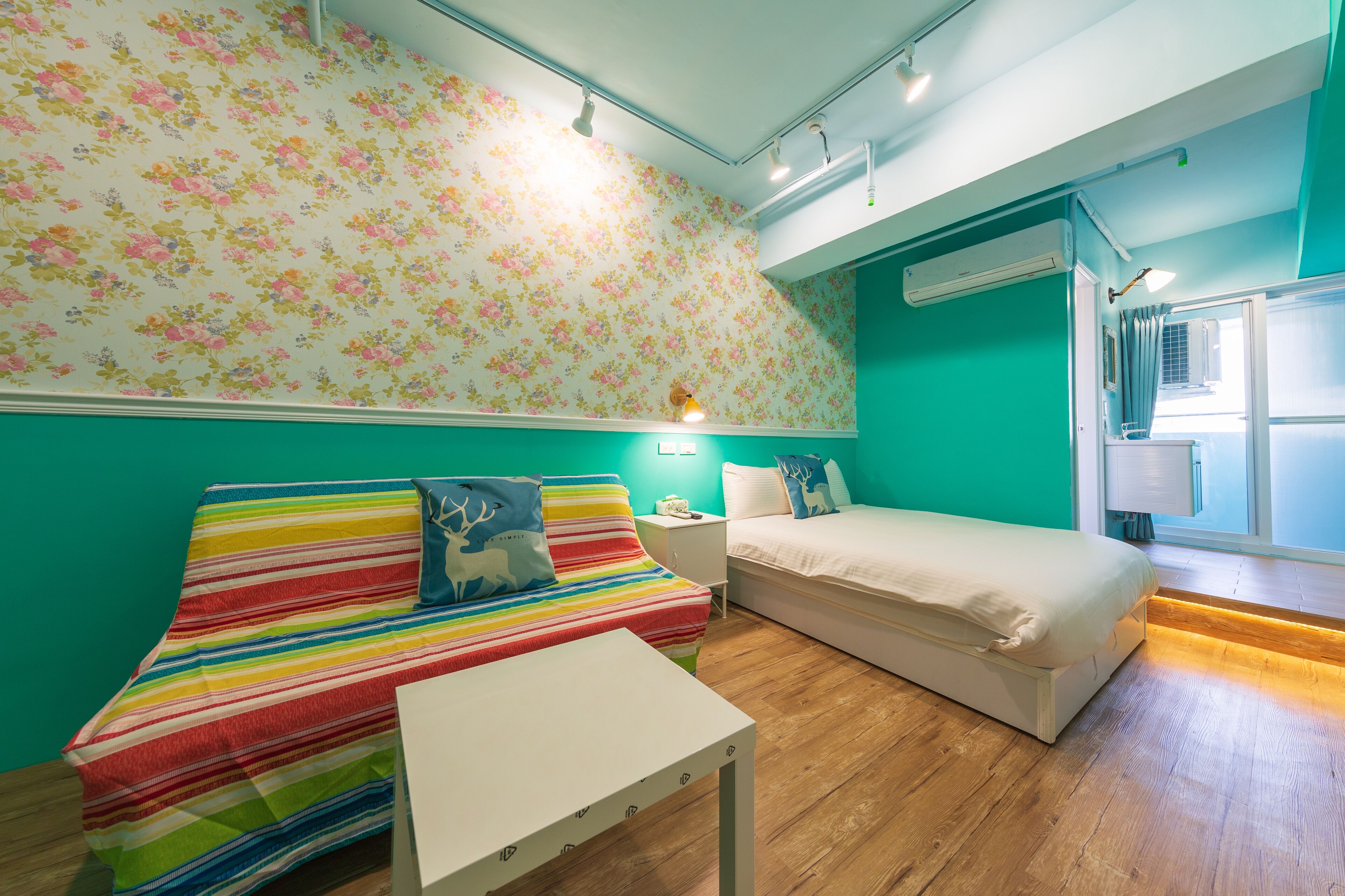 A room with a striped sofa, a bed, a small table, and a floral wallpaper.