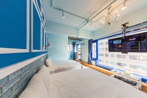 A hotel room with two beds, a TV displaying a digital board, and a window with a view of buildings. - I Hi Hotel (Kaohsiung)