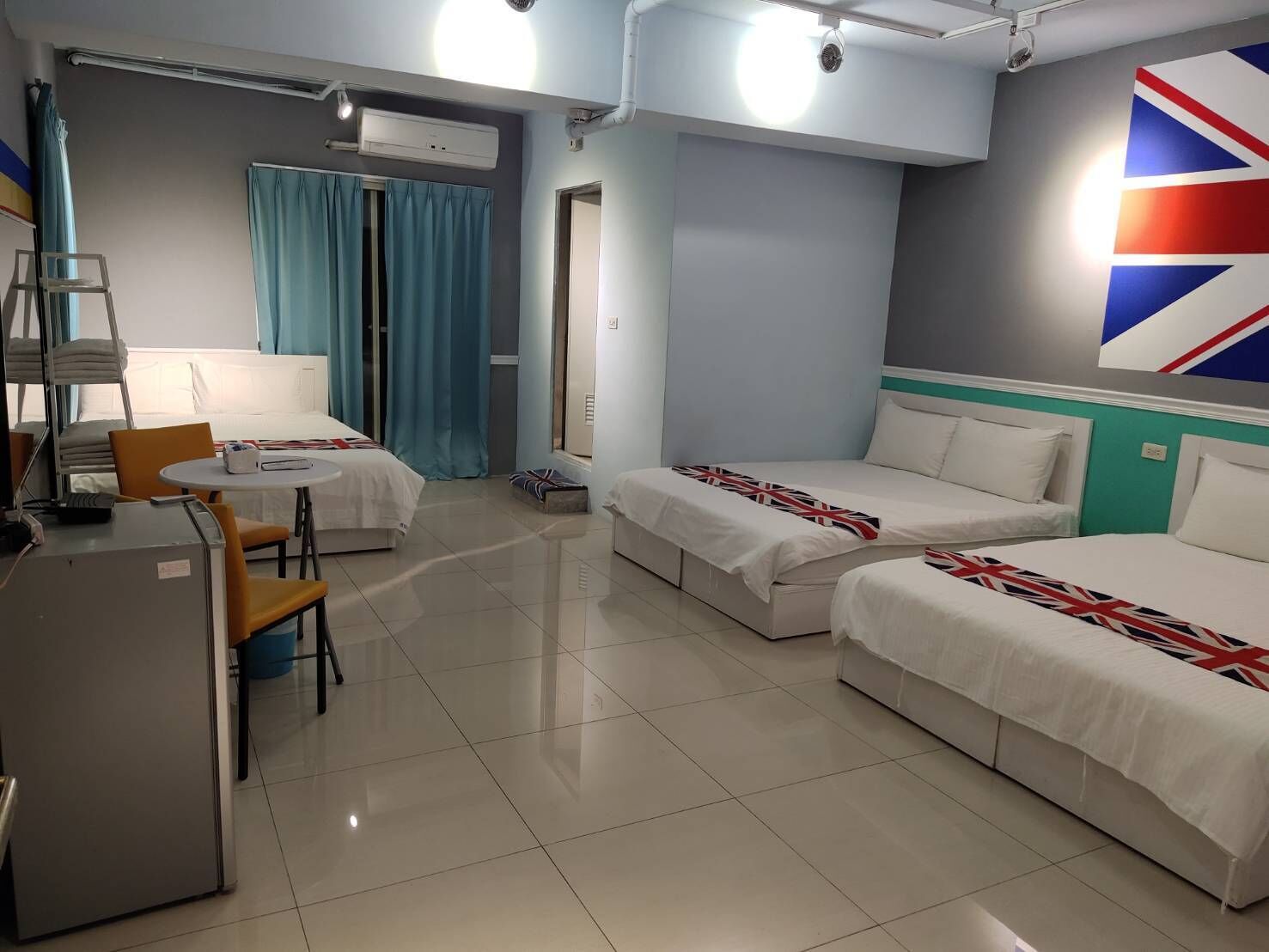A hotel room with two beds, a desk, a chair, and a window with curtains.
